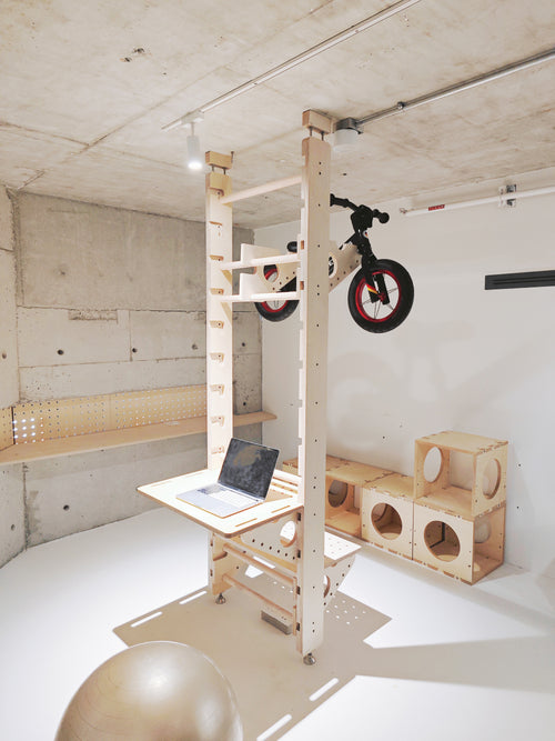 Floor-to-ceiling multifunction stall bars in birch plywood with tabletop; bicycle, extra shelves and props shown for styling